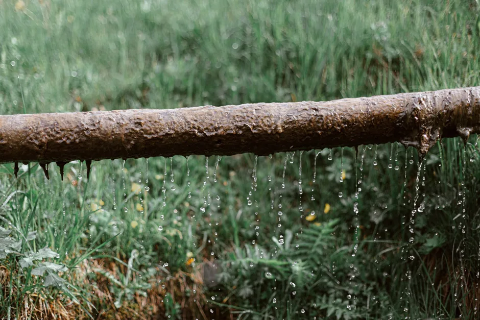 Water running steadily off a corroded pipe onto the grass below